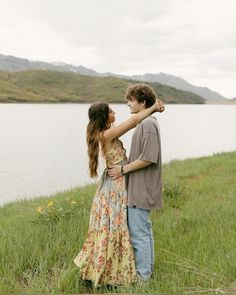 a man and woman standing next to each other in front of a body of water