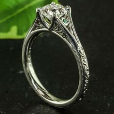 a close up view of a diamond ring on a black surface with leaves in the background