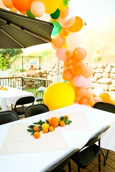 an outdoor dining area with tables, chairs and balloons in the shape of oranges