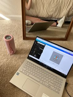 an open laptop computer sitting on top of a carpeted floor next to a mirror