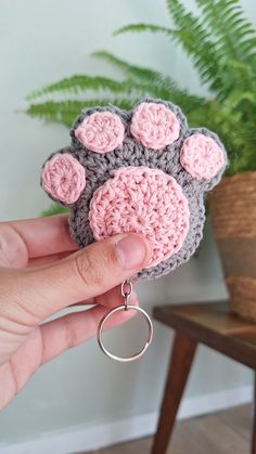 a hand holding a crocheted keychain with a dog paw on it