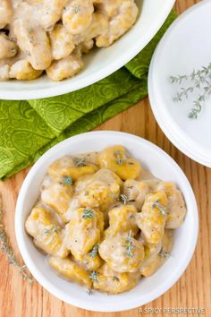 two bowls filled with chicken and cheese covered in gravy on top of a wooden table