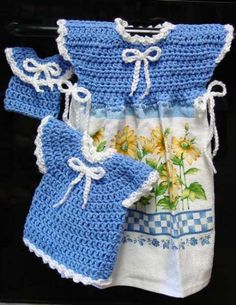 three crocheted baby clothes are displayed on a black surface with white and blue trimmings