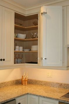 an open cabinet in the corner of a kitchen with white cabinets and granite counter tops