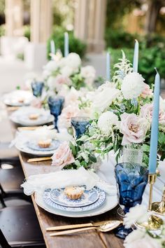 a long table set with blue and white plates, flowers and candles on top of it