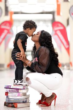 a woman kneeling down to kiss a small child on top of books in front of her