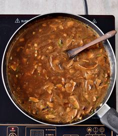 a pan filled with food sitting on top of a stove next to a wooden spoon