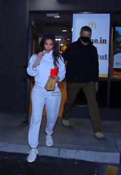 a man and woman are walking down the street in front of a mcdonald's