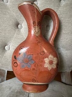 a red vase sitting on top of a chair next to a white pillow with flowers painted on it