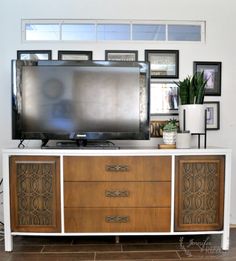 a tv is sitting on top of a dresser in front of a wall with pictures