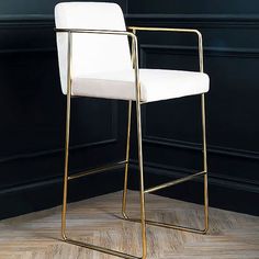 a white and gold bar stool sitting on top of a hard wood floor next to a black wall