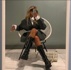 a woman sitting in a chair taking a selfie with her cell phone while wearing black boots