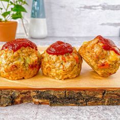 three mini muffins with ketchup are on a cutting board next to a potted plant