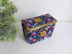 a small floral print box sitting on top of a table next to a potted plant