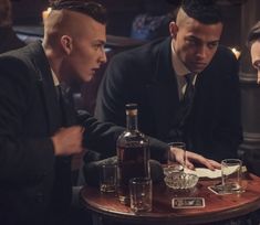 three men are sitting at a table with drinks in front of them and one man is looking down