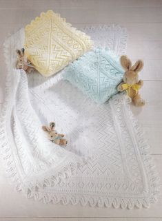 two stuffed animals laying on top of a white crocheted blanket next to each other