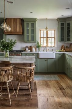 a kitchen filled with lots of green cabinets and wooden chairs next to a white counter top