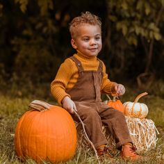 a young boy sitting on top of a hay bale next to two pumpkins