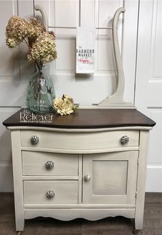 a white dresser with flowers and a vase on top