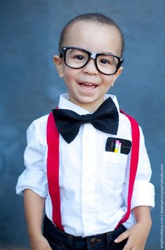 a young boy wearing glasses and a bow tie smiles at the camera while standing in front of a blue wall