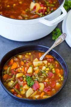 a bowl of vegetable soup with a spoon in it next to another bowl full of vegetables