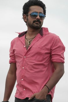 a man with sunglasses standing in front of the camera wearing a pink shirt and black pants