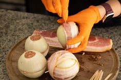 a person in orange gloves is peeling an onion on a plate with garlic and meat