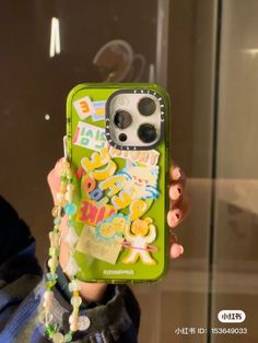 a person holding up a green phone case with stickers on it and beaded necklaces