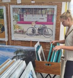 a woman is looking at paintings on display in a room with wooden crates and chairs