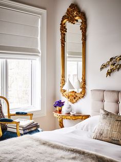 a white bed sitting next to a window in a bedroom under a gold framed mirror