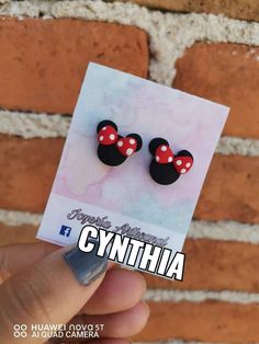 someone is holding up a pair of minnie mouse ear studs in front of a brick wall