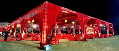 an outdoor wedding venue set up with red linens and lights on the sidelines