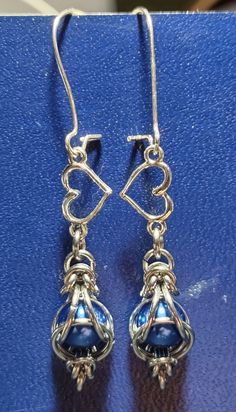 two blue glass beads hanging from silver earwires on a blue surface with heart shaped hooks