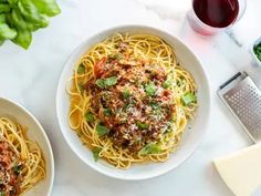 two white bowls filled with spaghetti and sauce next to parmesan cheese on a marble table