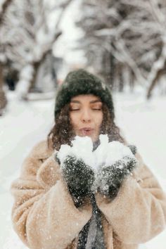 a woman blowing snow with her hands in front of her face while she is outside