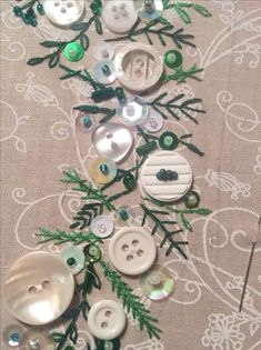 some buttons are laying on a table with green and white decorations around them, along with pine needles