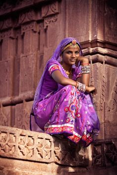 a woman in a purple dress sitting on a ledge