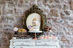 a white dresser topped with lots of cakes and desserts next to a wall mounted mirror