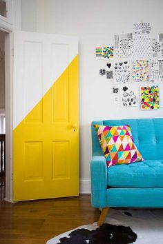 a bright blue couch in front of a yellow door and some pictures on the wall