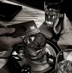 a person holding a credit card over a glass on a table with two cups and saucers