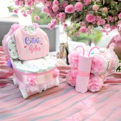 a table with pink flowers and baby items on it, next to a bouquet of roses