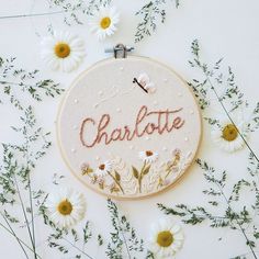 a hand embroidered name with daisies and daisies around it on a white surface