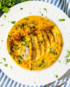 a white plate topped with chicken and yellow curry next to a fork on a blue and white striped table cloth