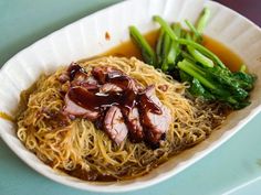 a white plate topped with noodles and meat next to broccoli on a table