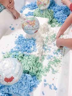 two children are playing in a bathtub filled with blue and green sprinkles