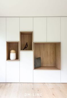 a white room with wooden shelves and two birds on the wall, one bird is sitting in the window