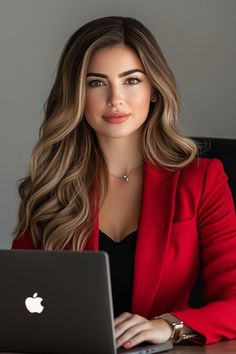 a woman sitting at a desk with a laptop in front of her and looking into the camera