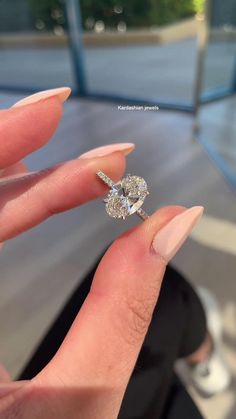 a woman's hand holding an engagement ring in front of her face, with the diamond