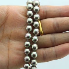 a person is holding some silver beads in their hand and there are two gold rings