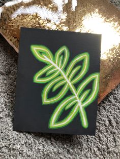 a green leaf painted on a black canvas next to a gold sequined pillow